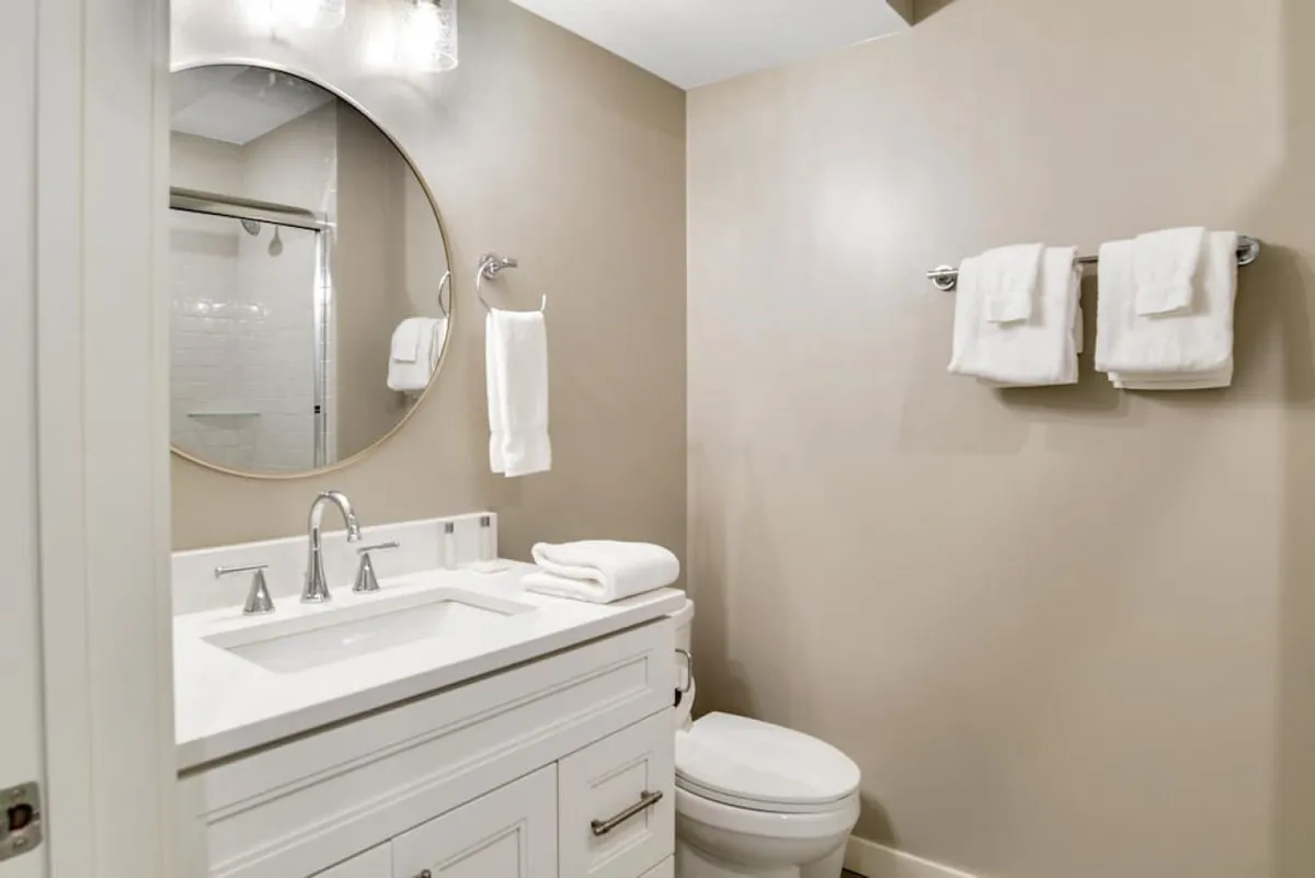 A contemporary bathroom with a round mirror, sleek sink, modern faucet, and plush white towels, all arranged in a clean, inviting layout. The space radiates calm and efficiency, perfect for morning and evening routines.