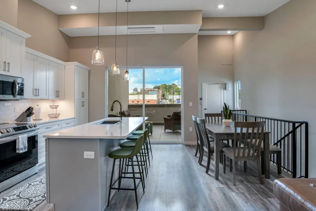 A modern kitchen and dining space with a central island, large window, and contemporary appliances. The space is open, inviting, and filled with natural light—suggestive of gatherings and casual entertaining just steps from the city.