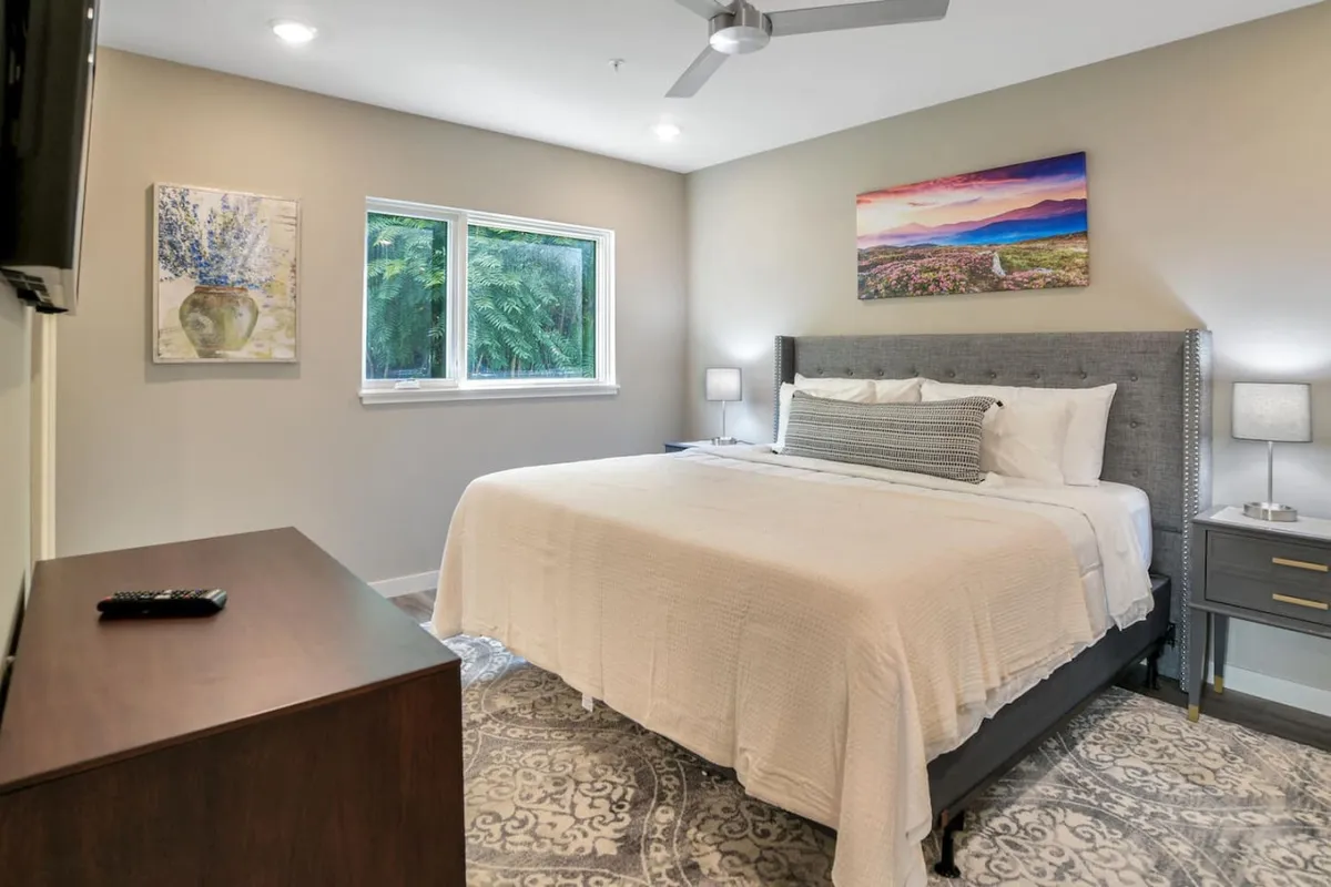 A serene bedroom scene featuring a comfortable bed, calming artwork on the wall, and a large window that lets in ample natural light. The overall ambiance is tranquil and inviting, ideal for relaxation and restful sleep.