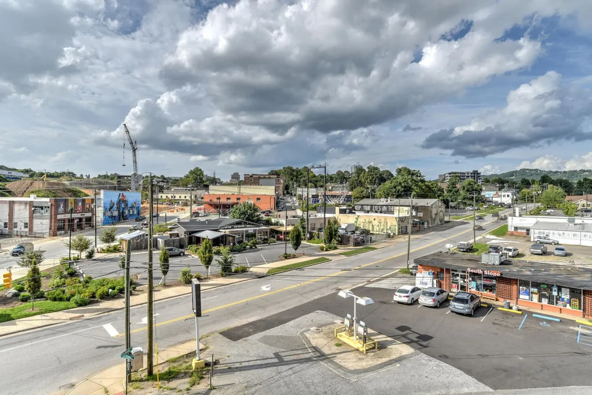 A lively street scene in Asheville’s South Slope, featuring buildings, pedestrians, and dramatic clouds overhead. The view captures the district's vibrant urban character, inviting passersby to explore the array of local attractions, shops, and street art.