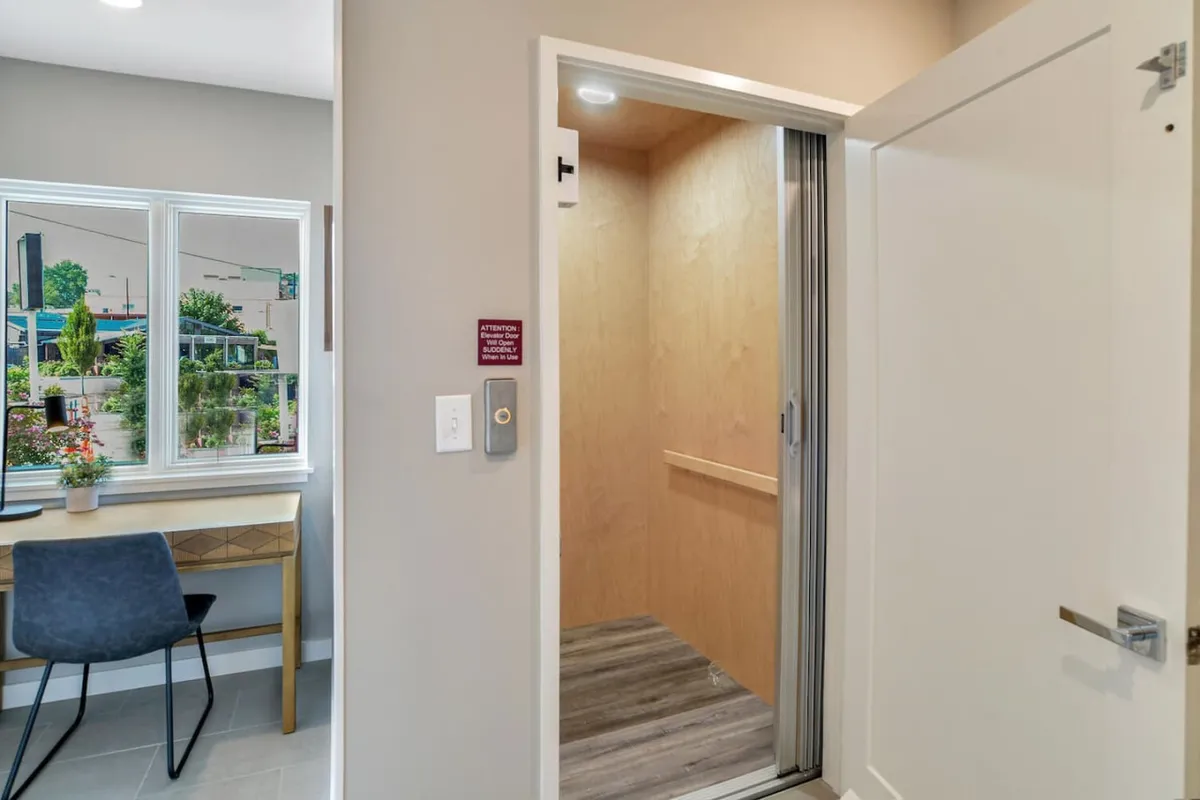A modern entryway featuring a sleek elevator, a tidy desk, and a bright window. The area is designed for practicality and style, setting a welcoming tone for the home from the moment you step inside.