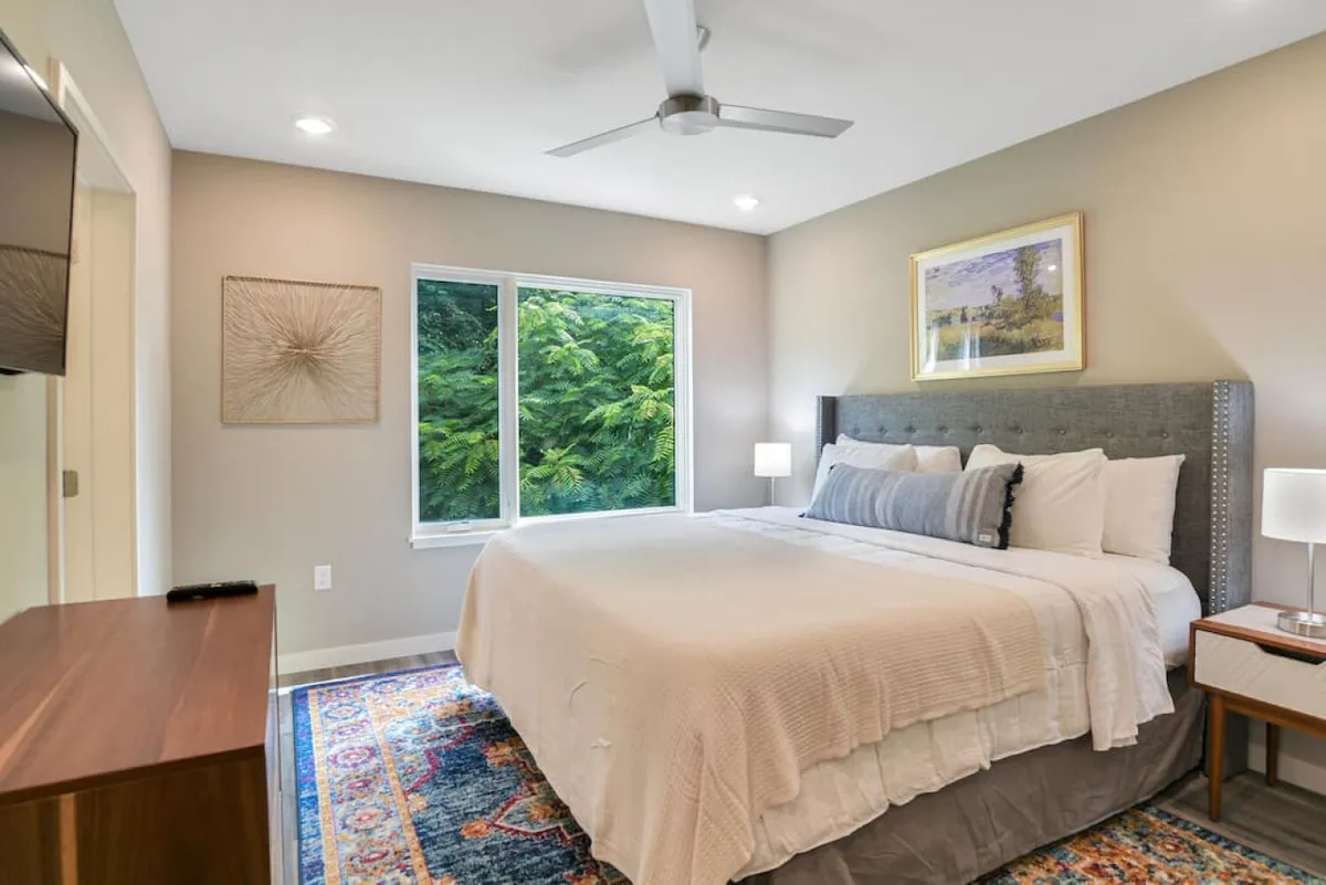 A serene king bedroom with a neatly made bed, a bright window that lets in natural light, a nightstand with thoughtful details, and a piece of art on the wall. The atmosphere is calm and inviting, perfect for restful nights and relaxing mornings.