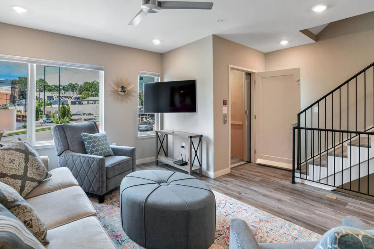 A cozy interior scene with a comfortable sofa, stylish ottoman, and large windows that flood the room with sunlight. The setup encourages curling up with a book, watching the sunset, or enjoying a peaceful afternoon.