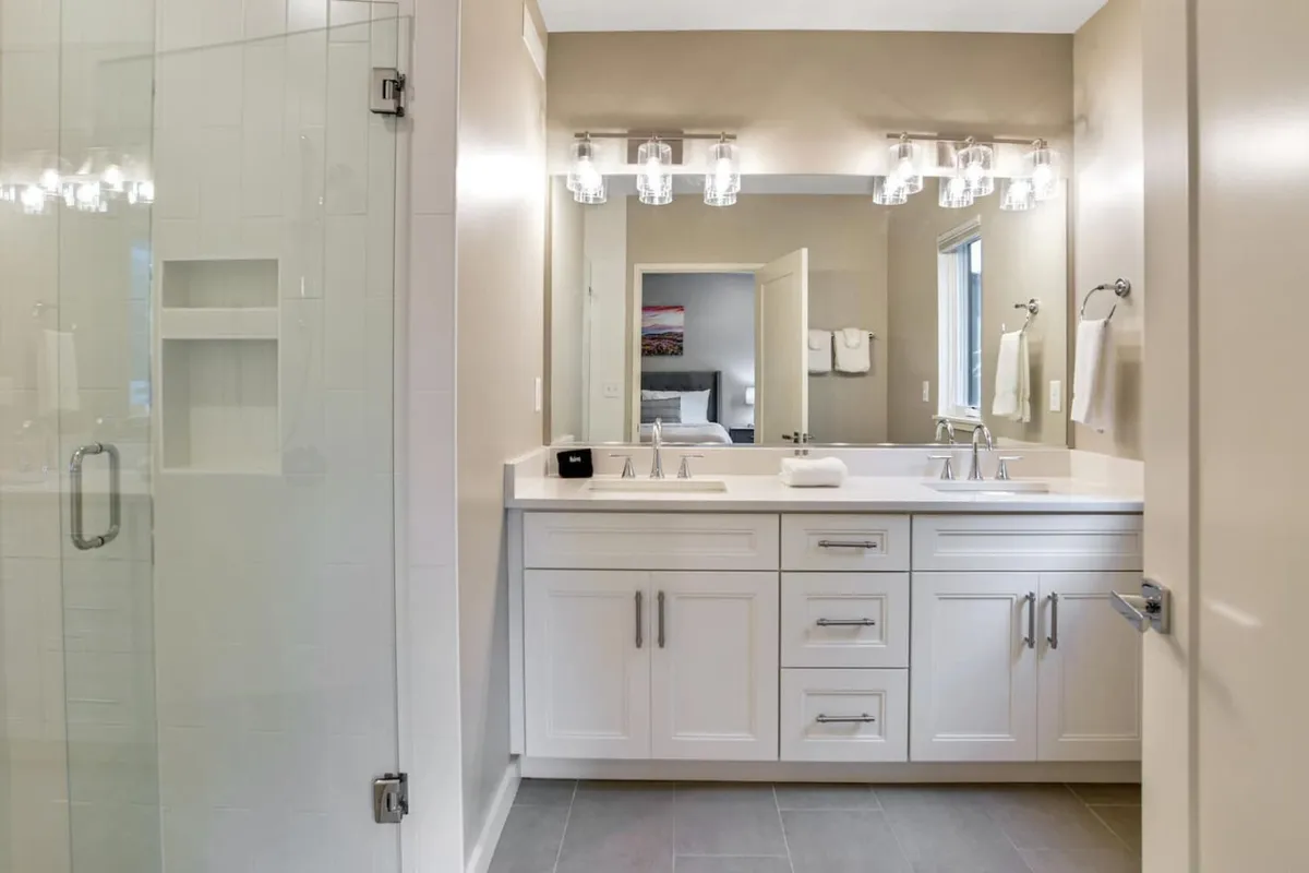 A modern, spacious bathroom featuring a double vanity, glass shower, and mirrored wall. The room is bathed in gentle light and invites moments of relaxation and self-care.